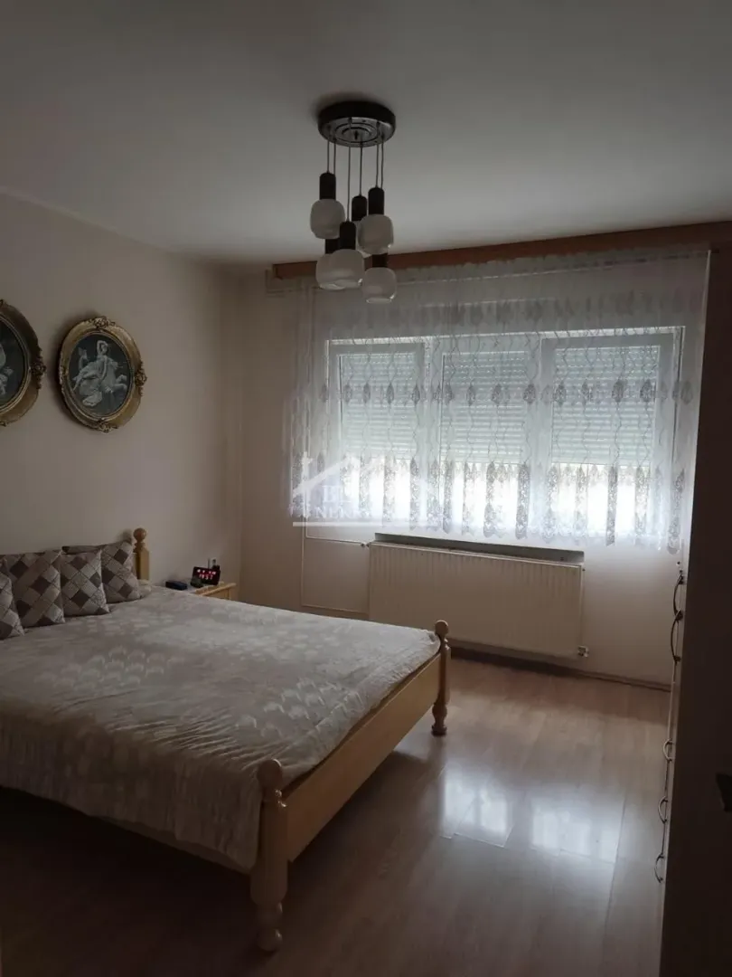 Nameštena spavaća soba sa bračnim krevetom, prozorom i lusterom.