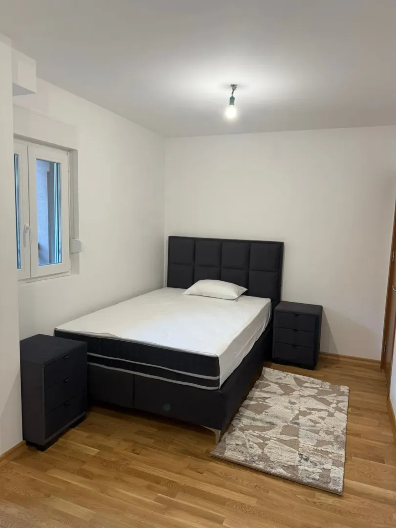 Spavaća soba sa bračnim krevetom, noćnim stočićima i laminatom.