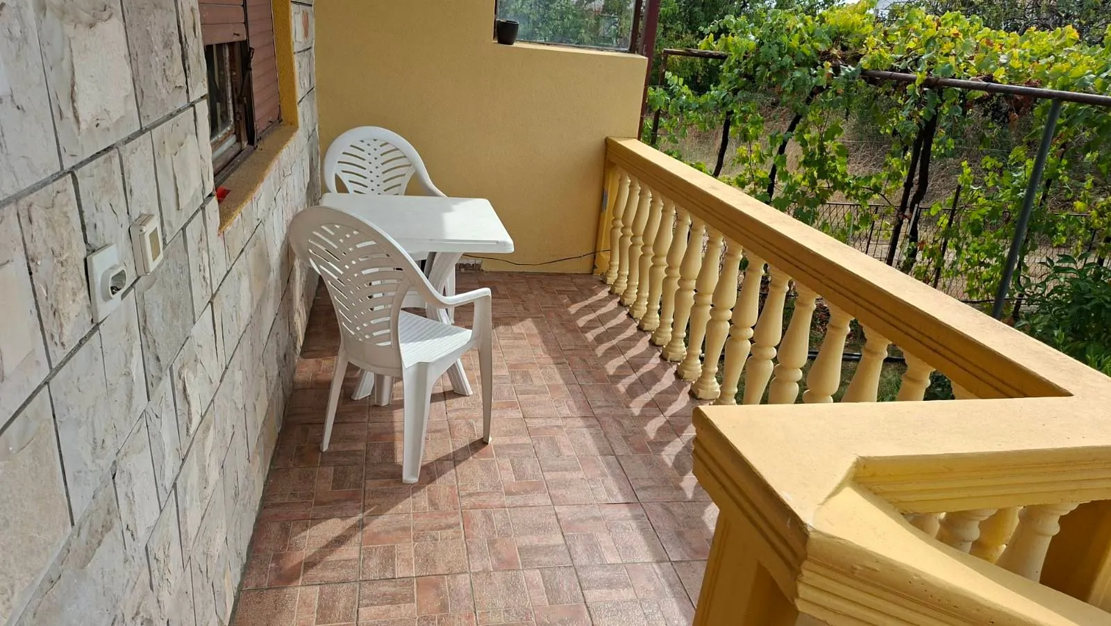 Natkriveni balkon sa garniturom za sjedenje i pogledom na zelenilo.
