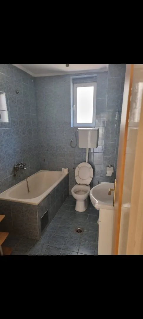 A bathroom featuring blue wall tiles, a bathtub, and a toilet.