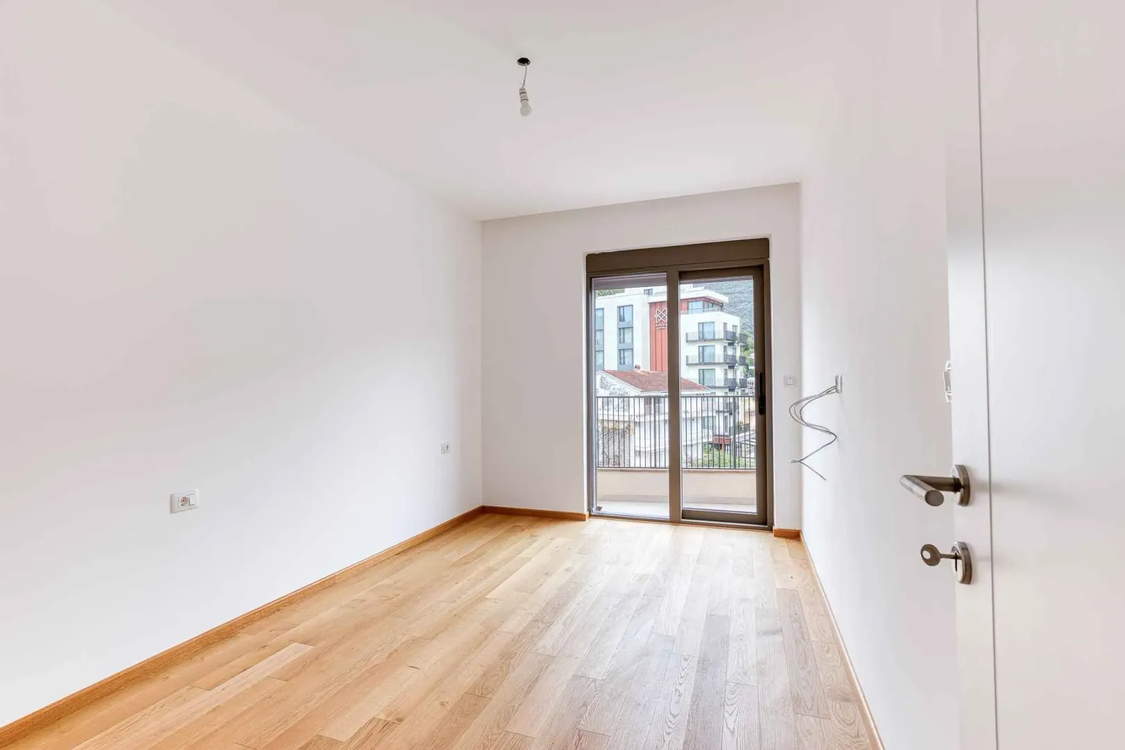 Prazna neopremljena soba sa drvenim podom i izlazom na balkon.