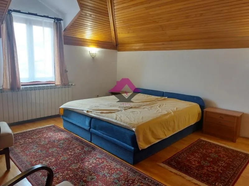 Spavaća soba sa bračnim krevetom i drvenim plafonom pod kosinom.