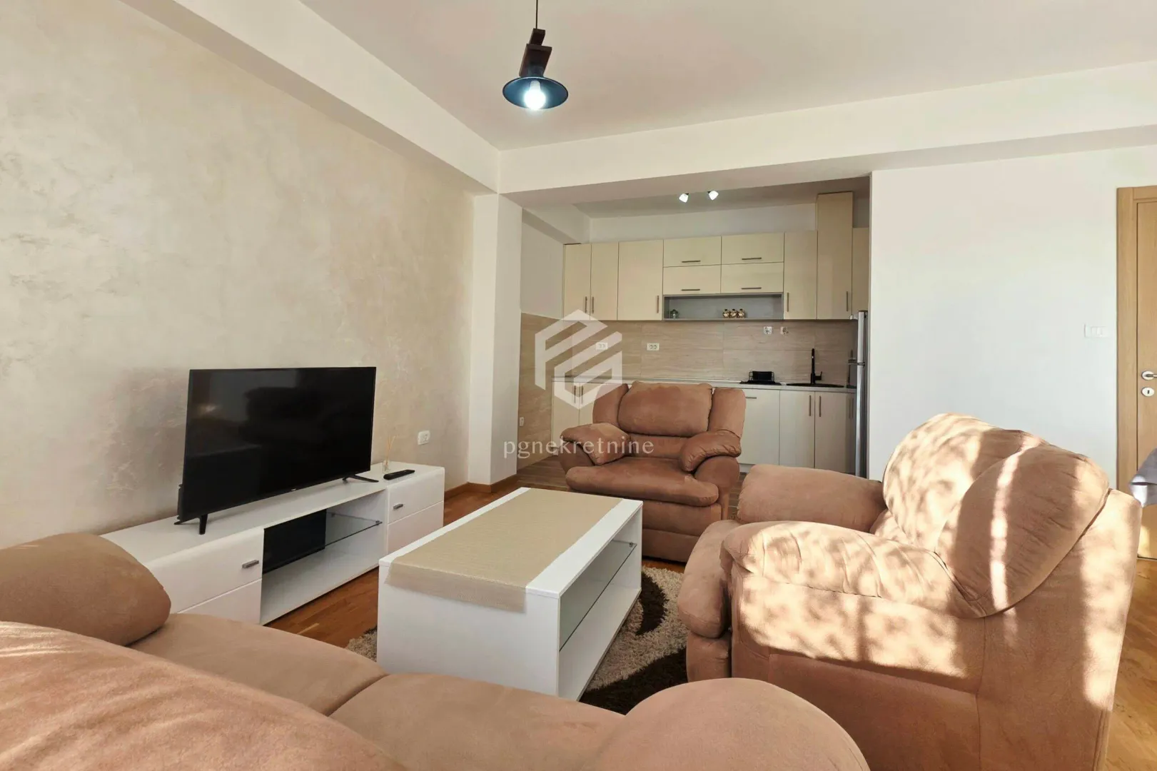 Living room with a sofa set and television, overlooking a smaller kitchen in the background.