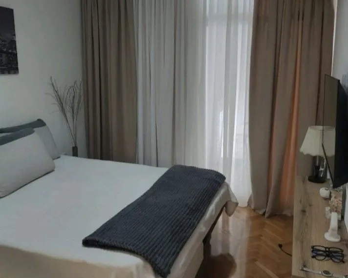 Furnished bedroom with a double bed and a window with curtains.