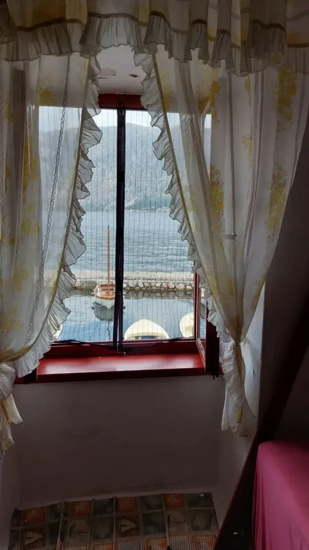Pogled kroz prozor sa zavesama na more i brodiće.