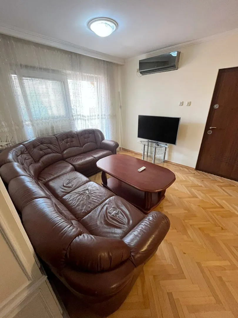 Dnevna soba sa kožnom garniturom, stočićem, televizorom i klima uređajem.