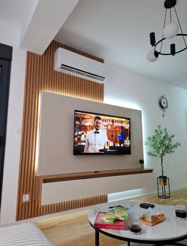 Dnevna soba sa TV panelom, drvenim oblogama i klima uređajem.