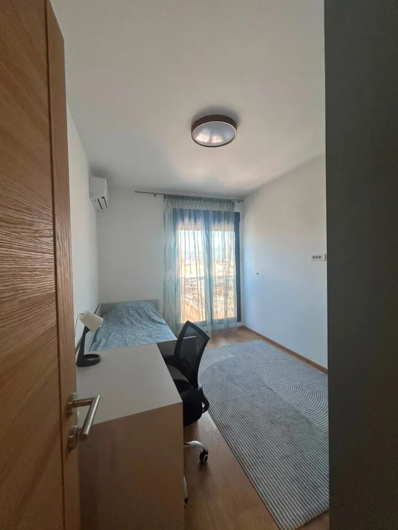 Small bedroom with a bed, desk, and window.
