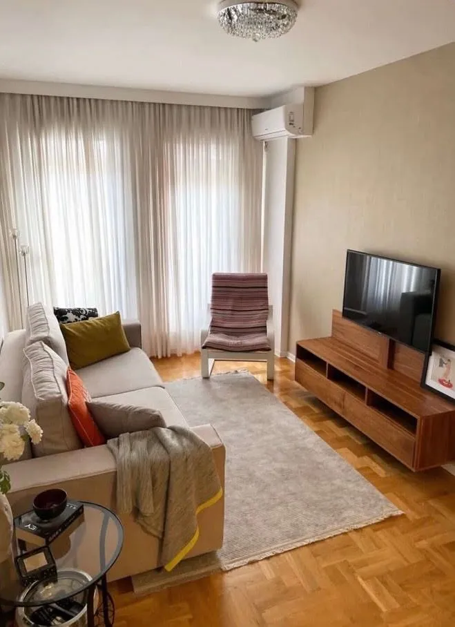 Furnished living room with sofa, TV and parquet flooring.