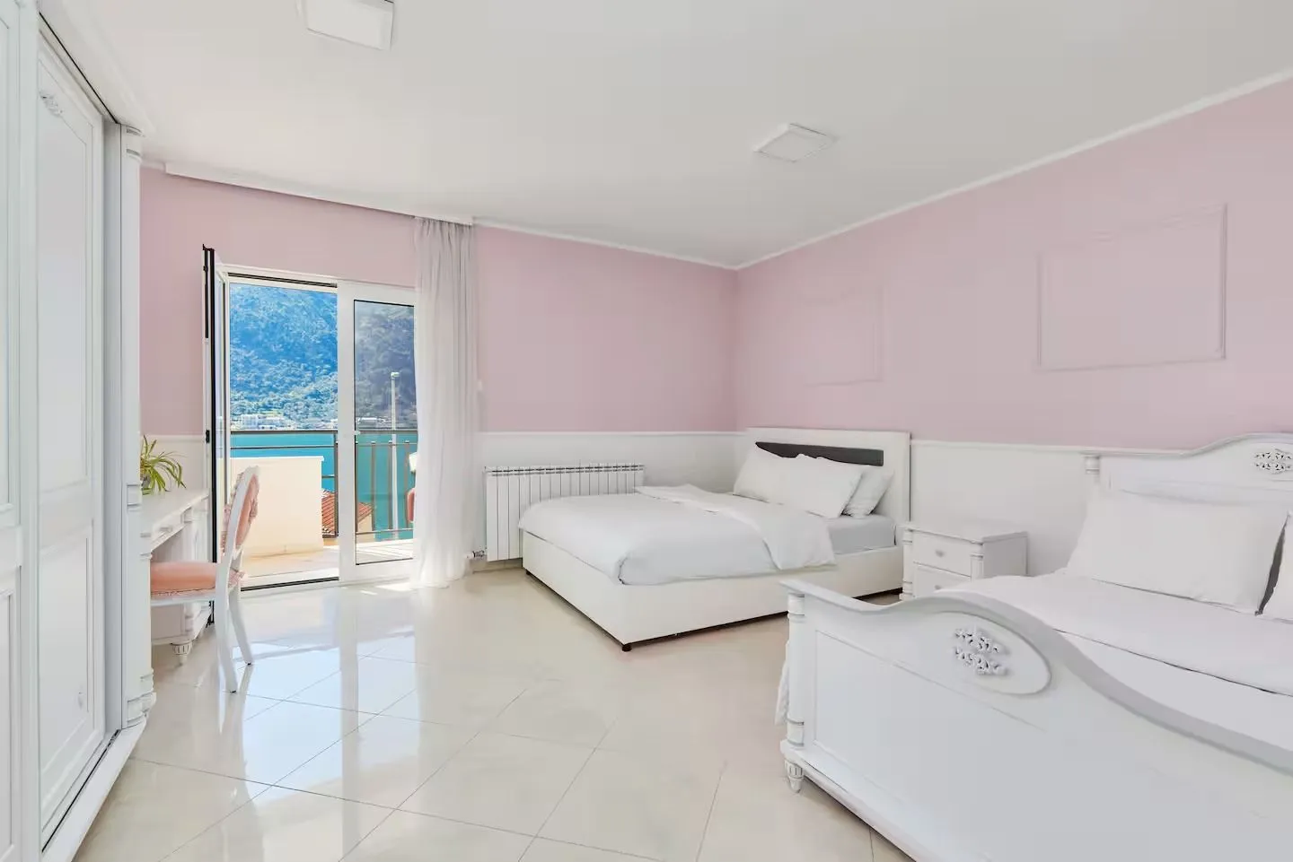 Spacious bedroom in pink and white tones with access to a balcony and sea view.