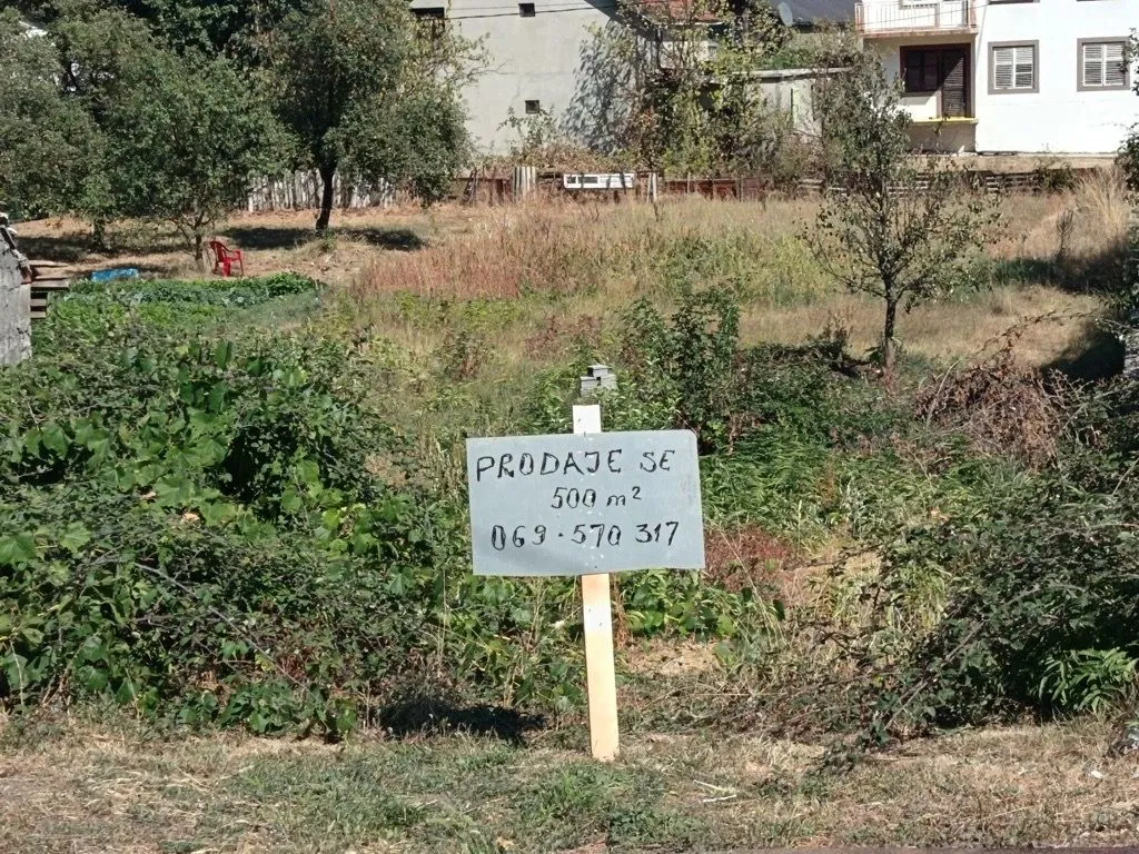 Zemljište sa znakom za prodaju i kućom u pozadini.
