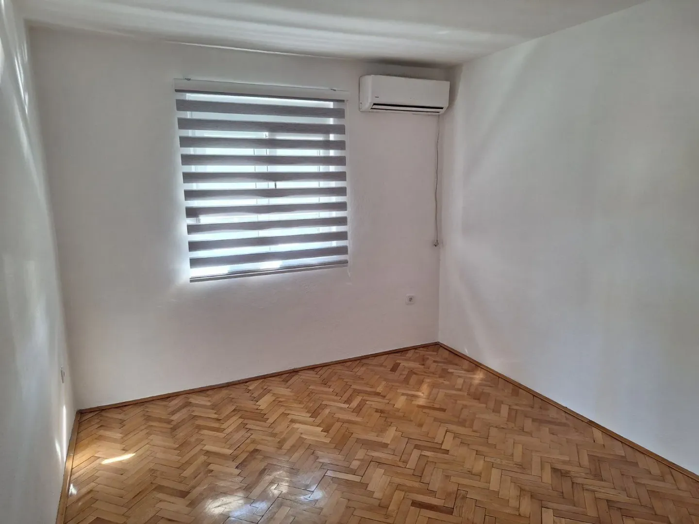 Empty room with parquet flooring and air conditioning.