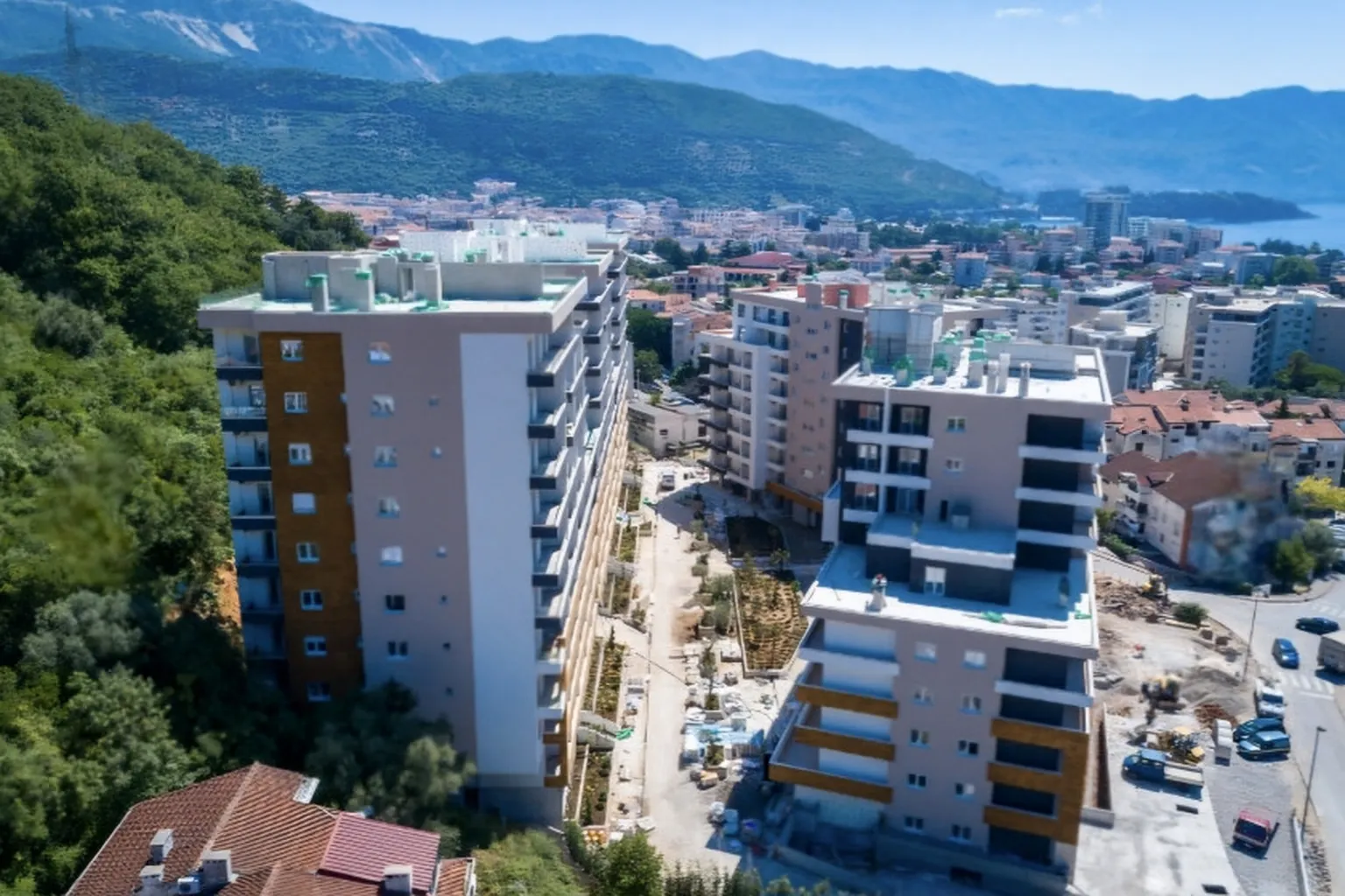 Pogled iz vazduha na stambeni kompleks u izgradnji i okolno naselje sa planinskim pejzažem.