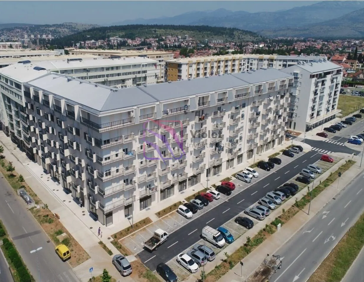 Pogled iz vazduha na stambenu zgradu sa okolnim parkingom i ulicom.