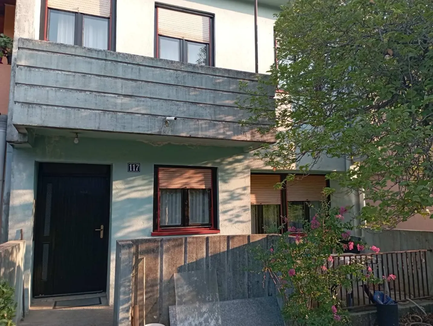 Fasada i ulaz kuće sa balkonom i dvorištem.