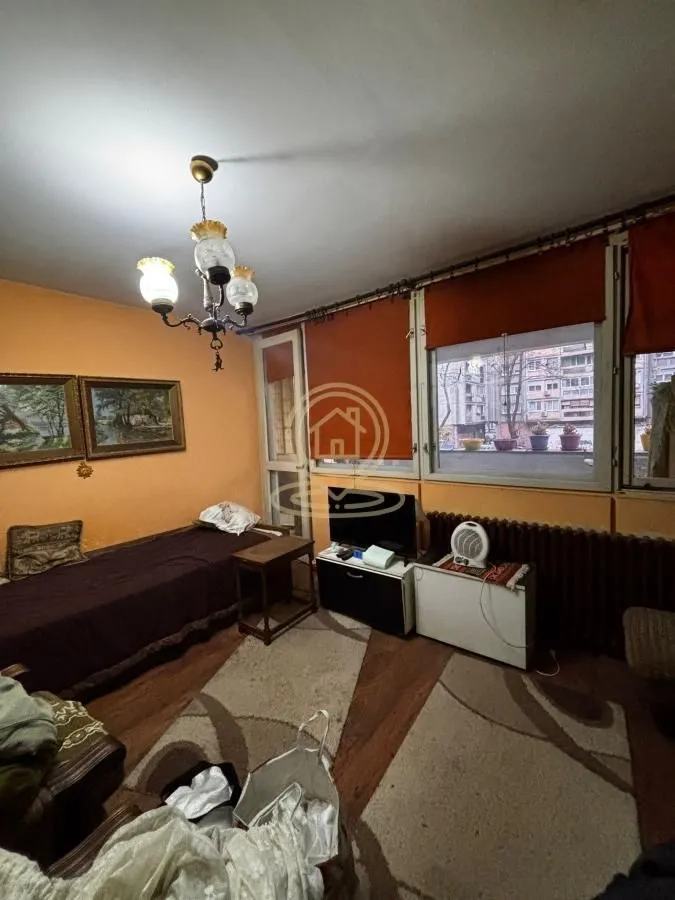 Manja spavaća soba sa krevetom, TV-om i velikim prozorima.