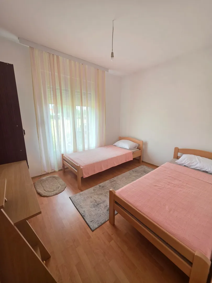 Bright bedroom with two wooden beds and a large window.