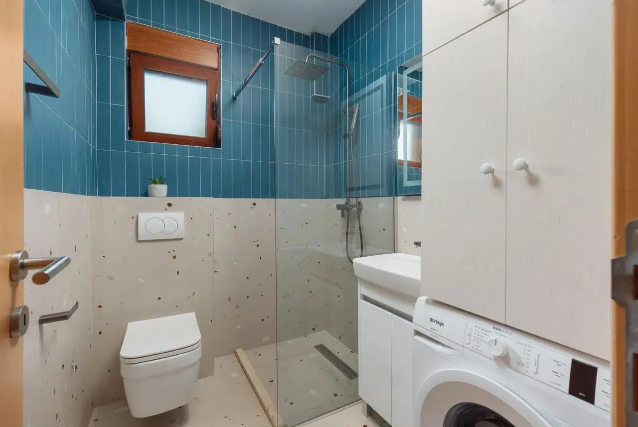 Modernly equipped bathroom with a shower cabin, washbasin, and washing machine.