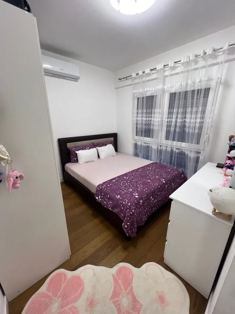 Namještena spavaća soba sa bračnim krevetom, bijelom komodom i klima uređajem.