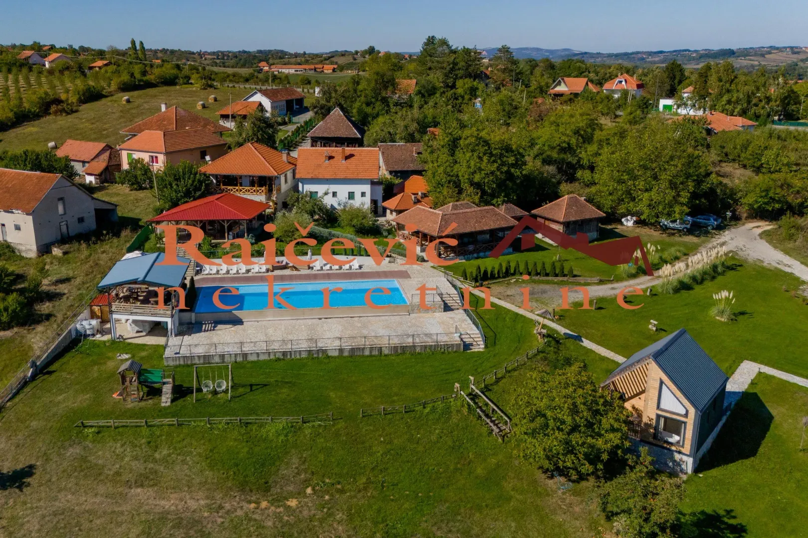 Pogled iz vazduha na imanje sa bazenom i kućama u prirodi.