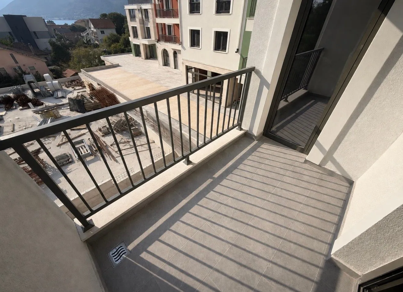 Manji balkon sa metalnom ogradom i pogledom na gradilište i okolne objekte.