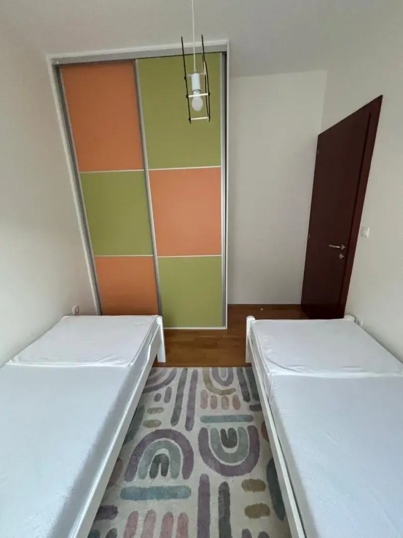 Children's bedroom with two single beds, a wardrobe, and a colorful rug.