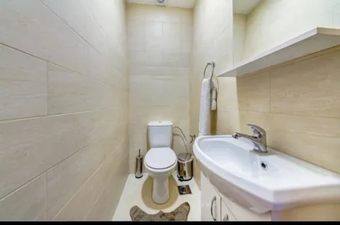 Manje kupatilo obloženo svijetlim pločicama sa toaletom i umivaonikom. - image 4