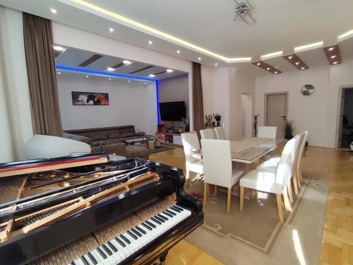 Spacious living room with sofa set, dining area, and a piano in the foreground.