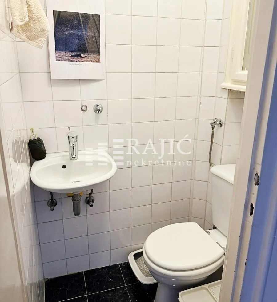 Smaller bathroom with white tiles, washbasin and toilet.