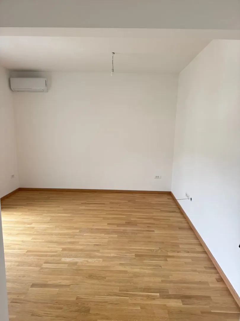 Empty room with wooden flooring and an air conditioning unit.