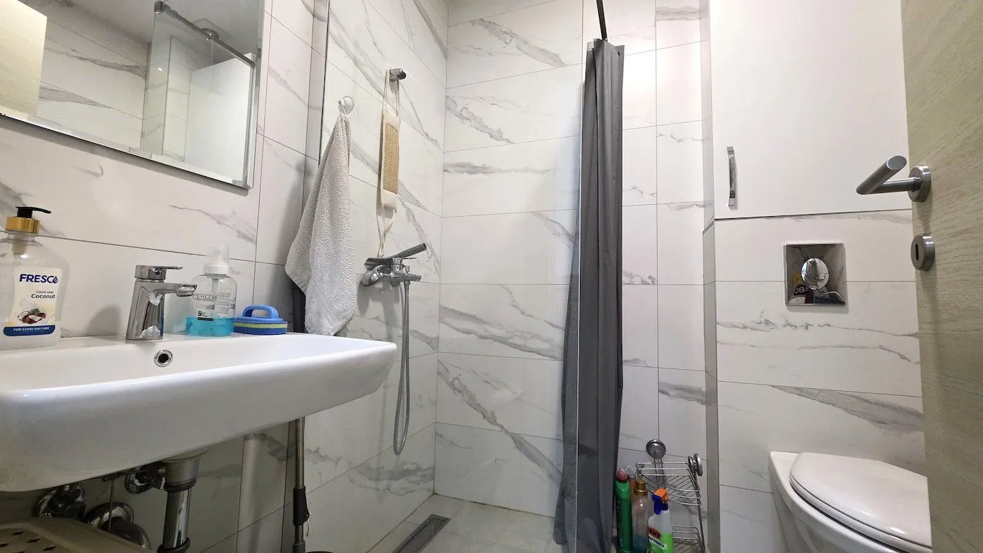Modern bathroom equipped with white marble tiles, a sink, and a shower cabin.