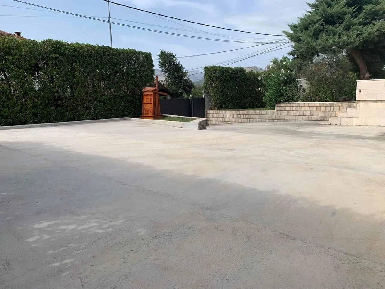 A spacious paved yard surrounded by a green hedge and a stone wall.