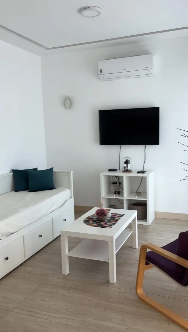 Bright living room with a sofa, TV, and white furniture.