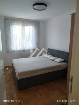 Spavaća soba sa bračnim krevetom, parketom i prozorom sa zavesama. - image 6