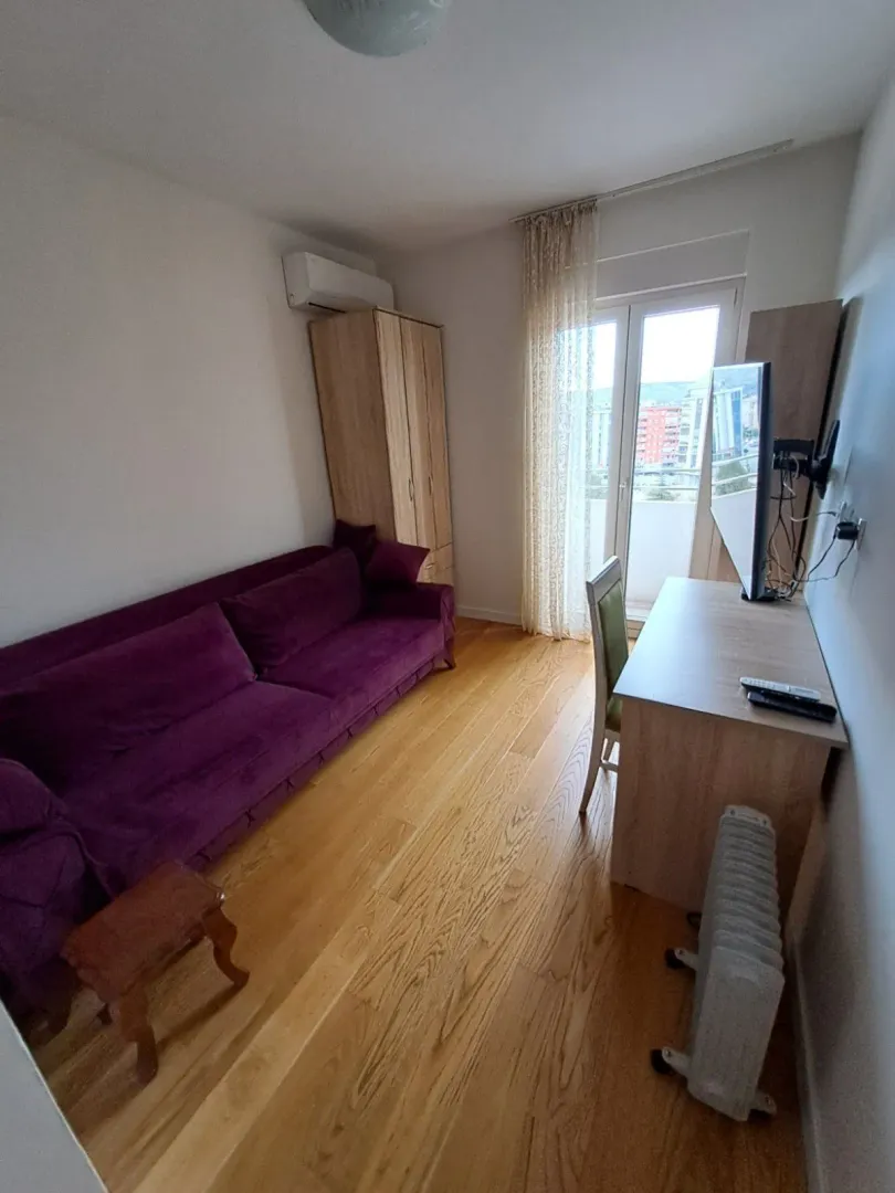 Svijetla dnevna soba sa ljubičastim kaučem, radnim stolom i izlazom na balkon.