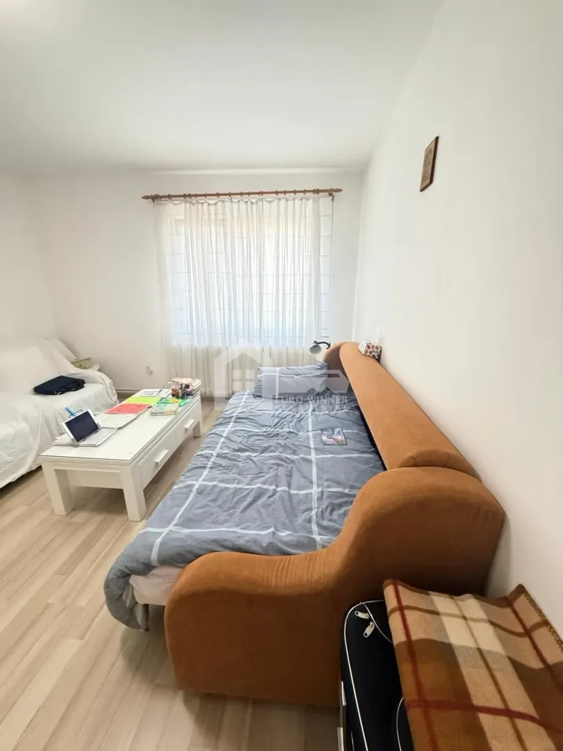Dnevna soba sa kaučem, foteljom, stočićem i prozorom sa zavesama.