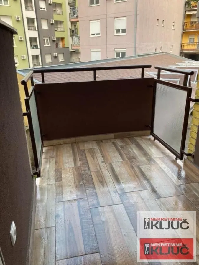 Otvoreni balkon sa popločanim podom i metalnom ogradom.