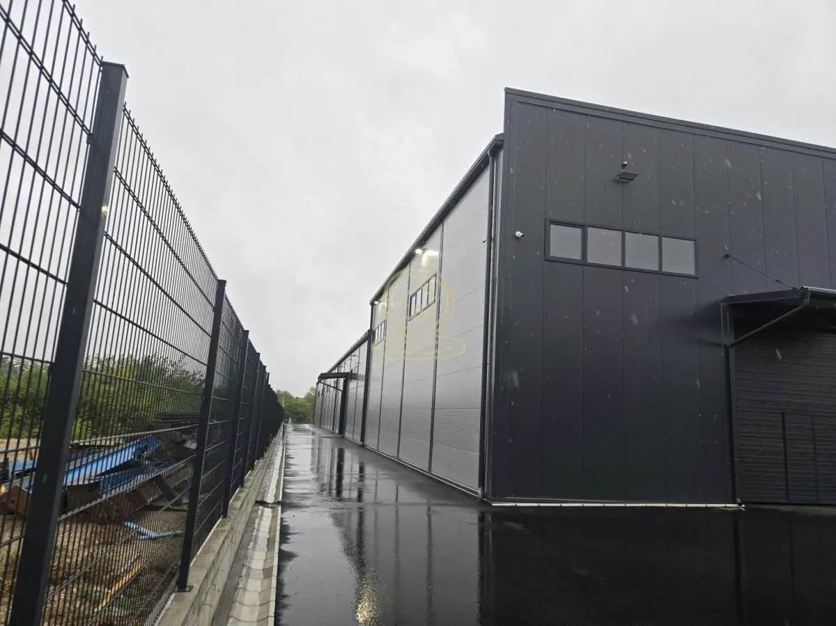View of the exterior of an industrial building with a fence and a concrete walkway.
