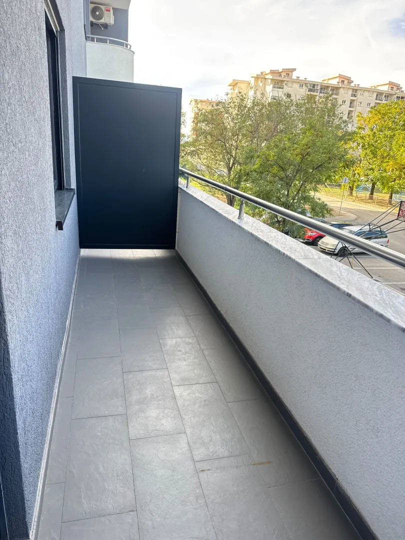 Prostrana popločana terasa sa metalnom ogradom i pogledom na naselje.