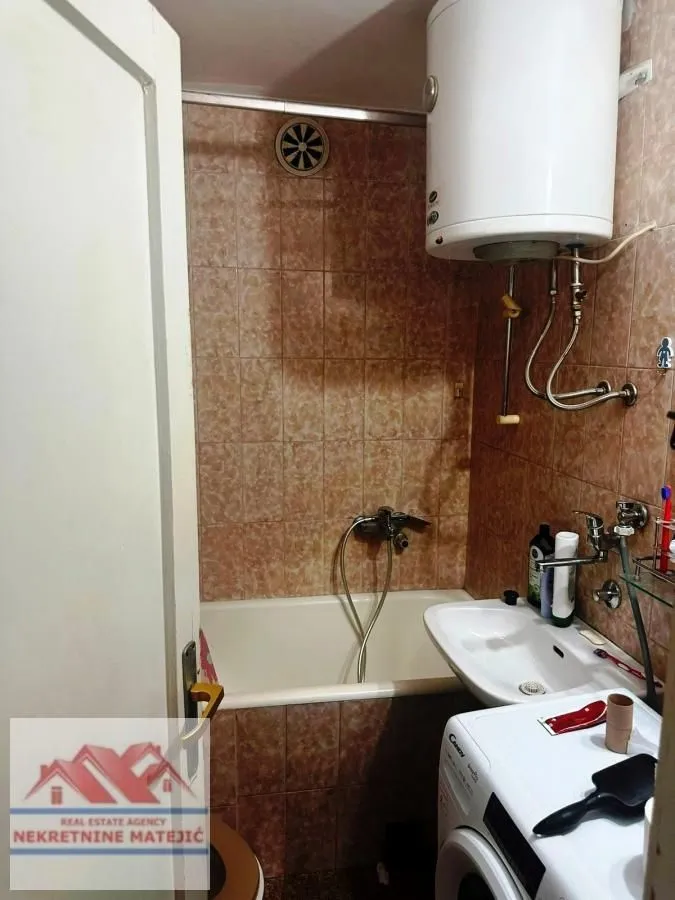 Smaller bathroom with a bathtub, washbasin, water heater, and washing machine.