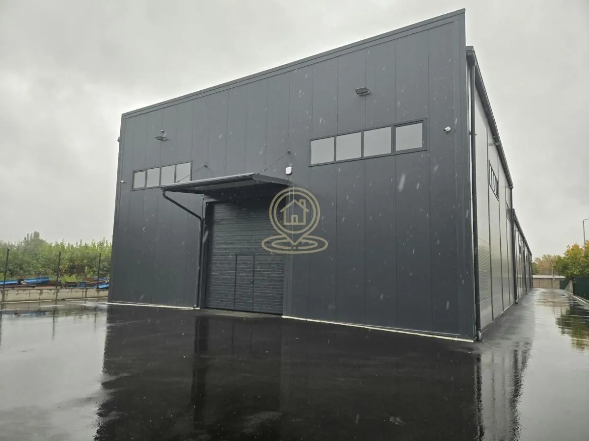 Exterior view of a modern industrial hall with a large door and paved courtyard.