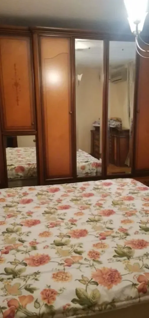 A bedroom with a large wooden wardrobe and a bed with a floral bedspread.