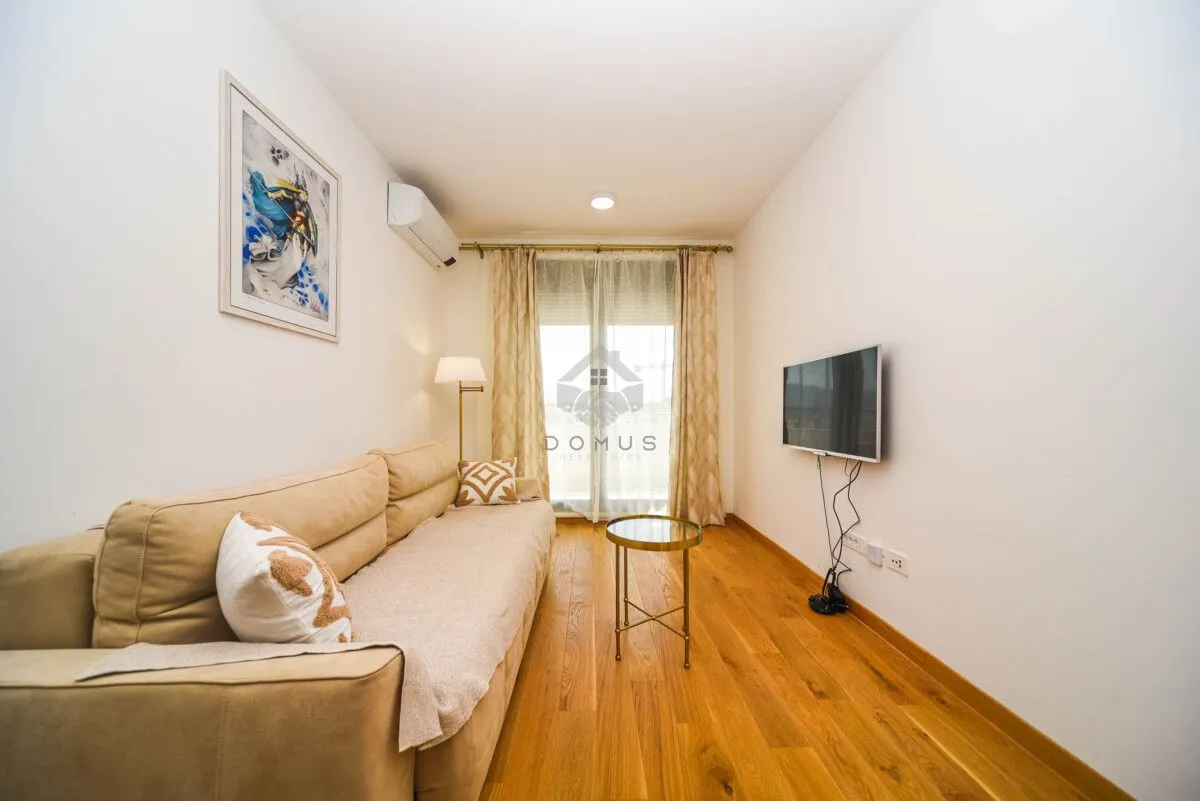 Small living room with a beige sofa, small coffee table, and wall-mounted TV.