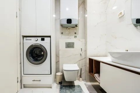 Modern bathroom with a washing machine, built-in cabinet, and water heater. - image 9