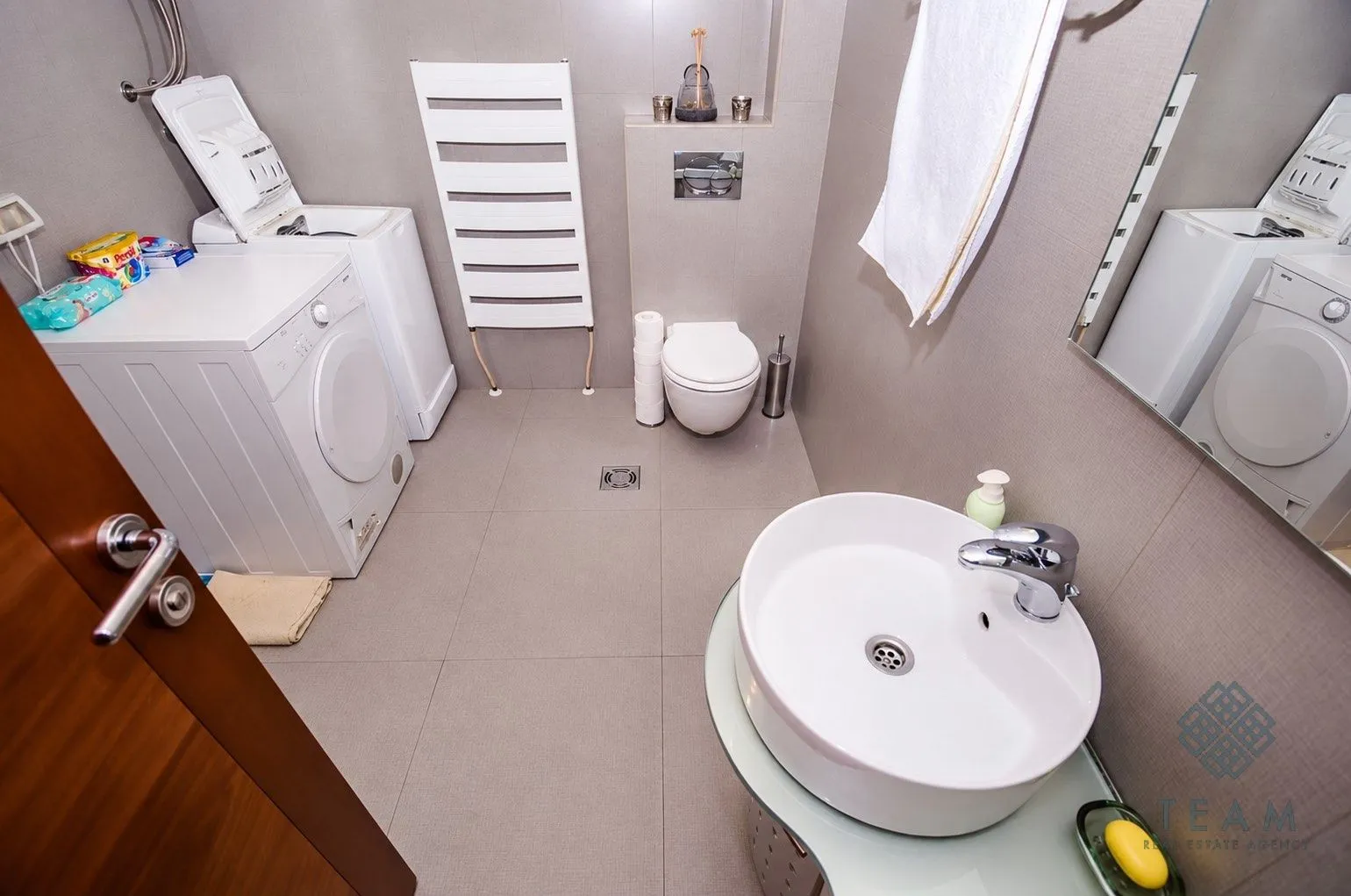 Moderno opremljeno kupatilo sa veš mašinom, WC šoljom i umivaonikom.