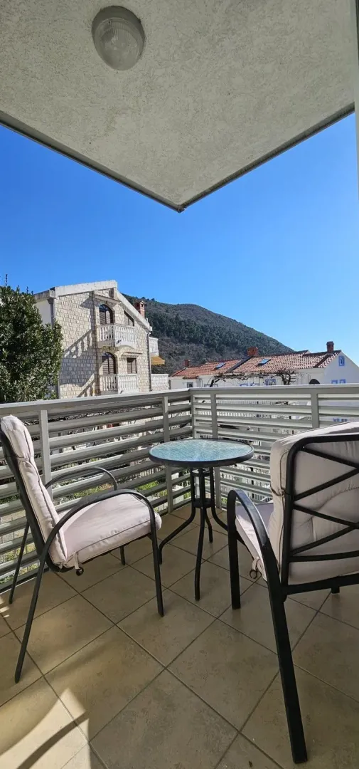 Covered terrace with seating furniture and a view of surrounding buildings and a hill.