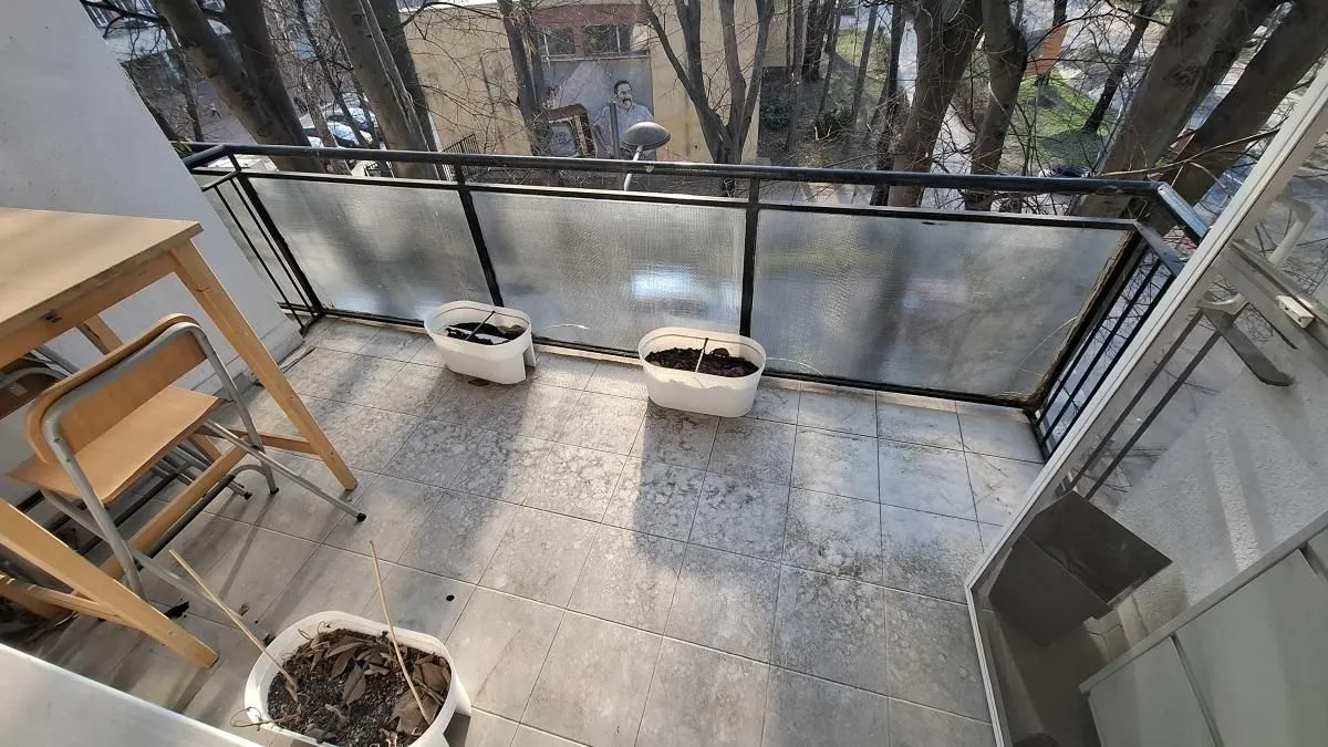 Manji popločani balkon sa crnom ogradom i saksijama za cveće.