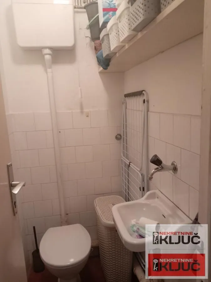 Manje kupatilo sa toaletom, umivaonikom i policama za odlaganje.