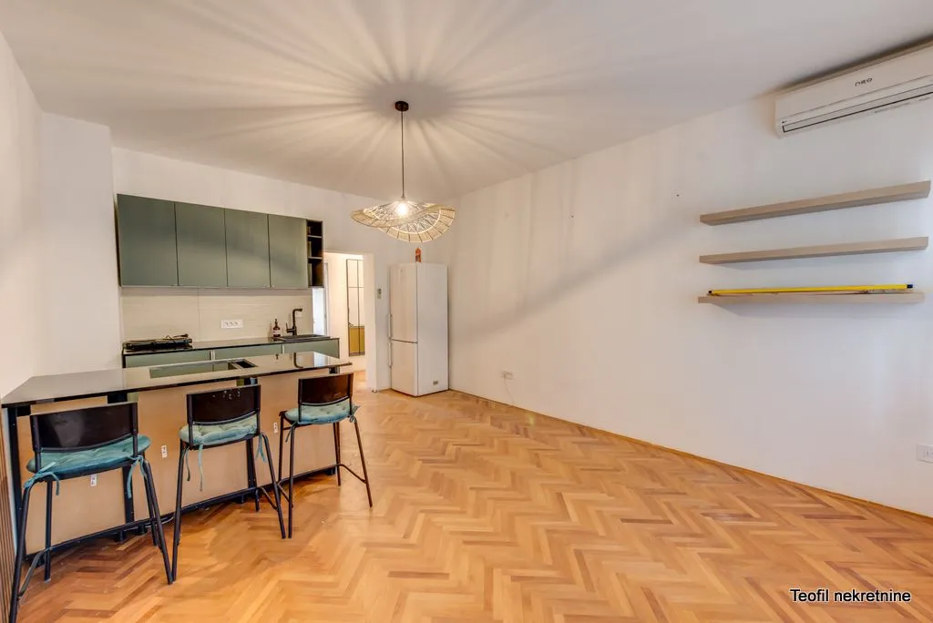 Living room with a kitchen and a bar counter, featuring wooden parquet flooring.