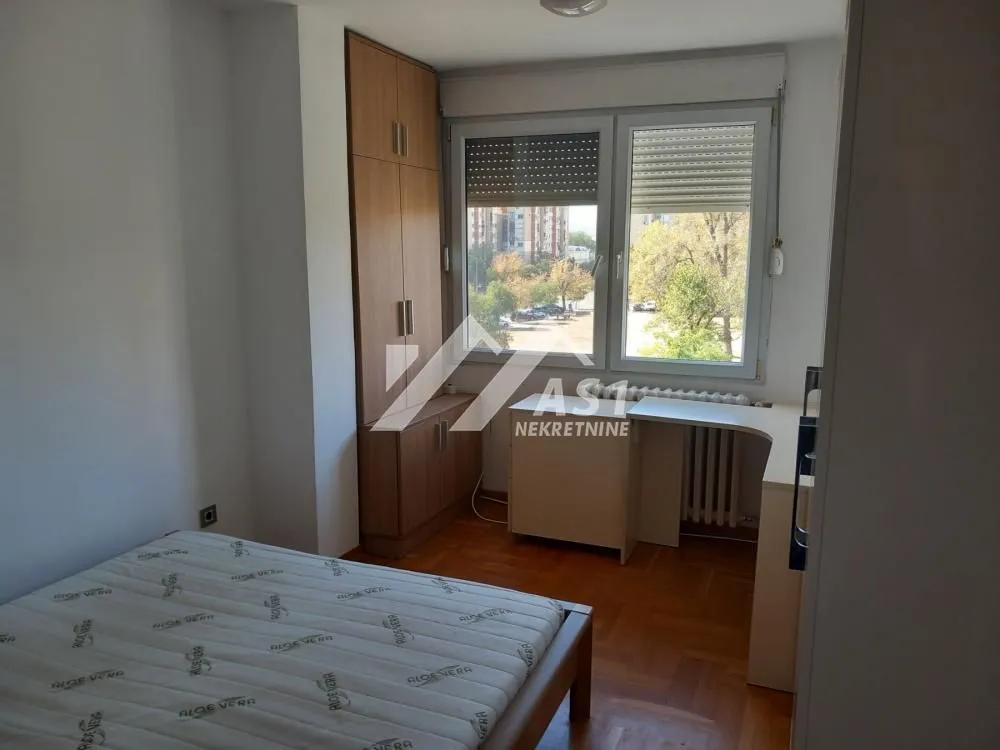 Furnished bedroom with a bed, fitted wardrobe, and a window overlooking the neighborhood.